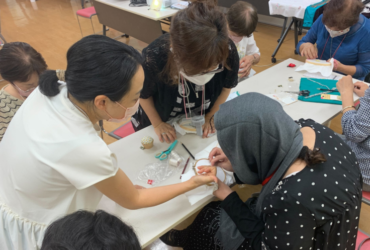 身を乗り出して、講師(手前・右)が刺繍する手元をのぞき込む参加者らの写真