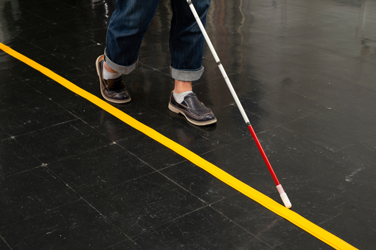 床に敷設されているココテープを、白杖で辿りながら歩いているスニーカーを履いた人の写真