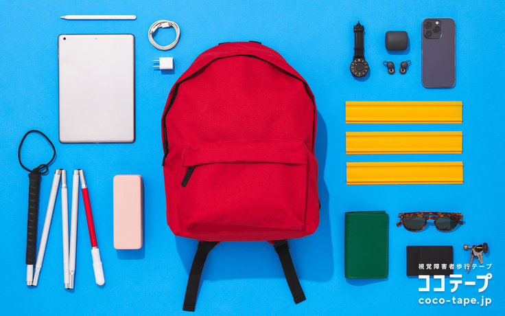 ココテープのビジュアル。水色の背景の真ん中に赤いリュックサック、その周りには、25cmの長さのココテープ3本、スマホ、時計、メガネ、白杖などの外出時のアイテムが整列して並べられている。