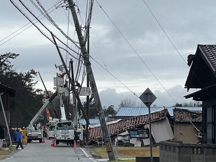 倒壊する家屋や、傾く電信柱と災害支援車両