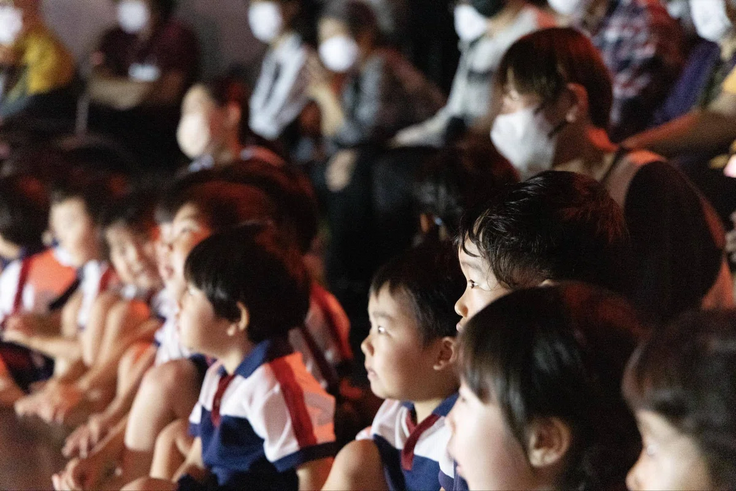 公開リハーサルで、保育園の子どもたちがアーティストのパフォーマンスを観ている様子。