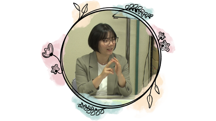 AIによるプロフィール写真の説明：この写真には、黒髪のショートボブの女性が写っています。髪はあごのあたりで切りそろえられていて、前髪があります。丸い縁のメガネをかけていて、顔立ちはやわらかく、優しい雰囲気です。  彼女は口を少し開けて笑顔で話しているような表情をしています。目はしっかりと開いていて、相手の話に興味を持ちながら話しているような印象です。  服装は、グレーのジャケットに白いインナーを着ています。  そして、両手を顔の前で軽く組むようにしながら、指先同士を軽く合わせています。ちょうど、人に何かを丁寧に説明しているときの手の動きに見えます。指の動きが柔らかく、落ち着いた話し方をしているような印象を与えます。  背景は室内で、薄いベージュの壁の前に座っています。