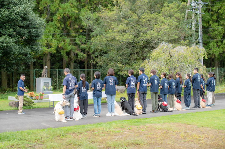 献花の様子。協会敷地内にある慰霊碑の前に横１列に並んでいる職員。