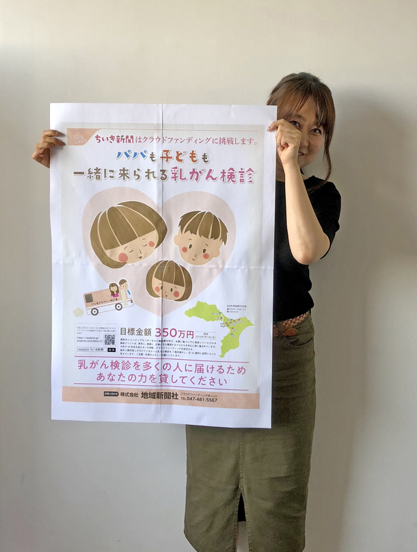 地域新聞社のピンクリボン運動として行っている乳がん検診実施のためのクラウドファンディングポスターを持つ社員