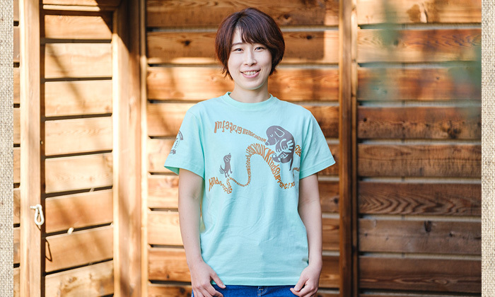 女性がライトグリーンのTシャツを着ている。胸元にロゴと、ブラックラブの子犬のイラスト。