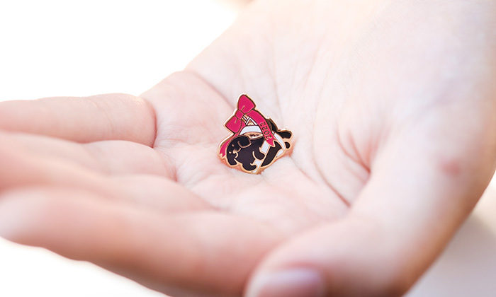 手の平にブラックラブのピンバッジが乗っている。パピーがハーネスを持っているデザイン。