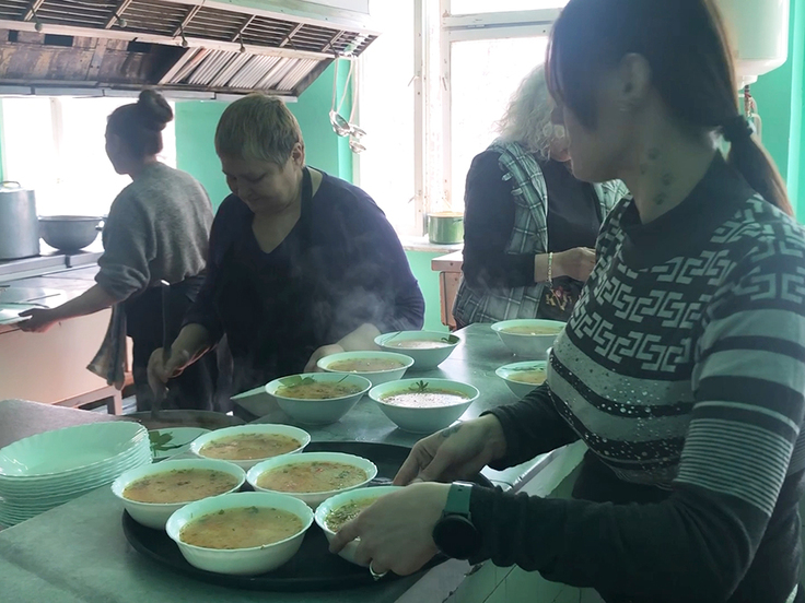 食事の皿をお盆に載せて難民のいるテーブルに向かう調理スタッフの女性