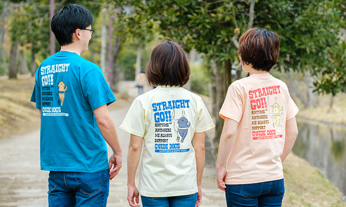 バックプリントのあるTシャツを着た男女が3人並ぶ写真。イラストは盲導犬